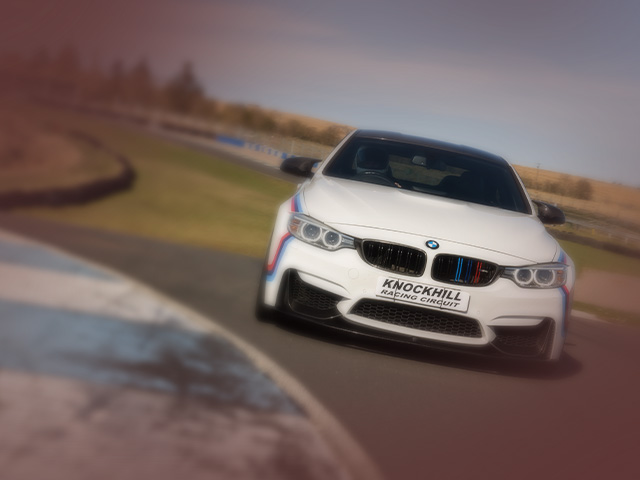 White BMW M4 car with red and blue stripes turing a bend on the Knockhill track